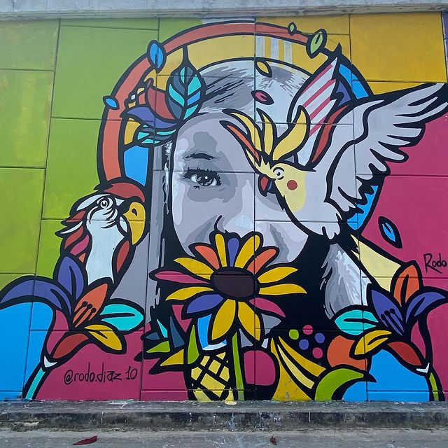 street art coloré d'une dame avec autour d'elle des fleurs et des perroquets 