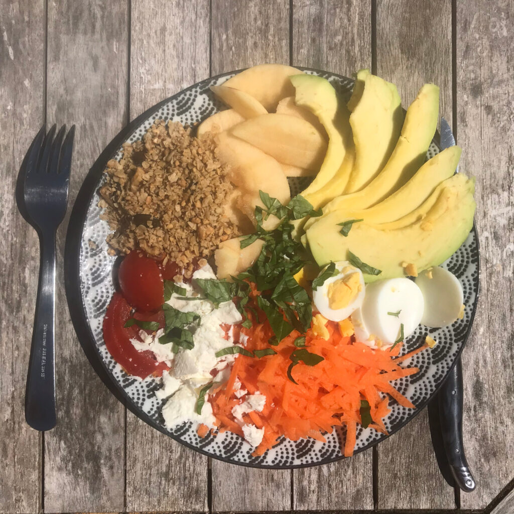 Assiette à motif qui contient des lentilles, des pommes, de l'avocat, des tomates, des oeufs, des carottes, du fromage et de la salade.